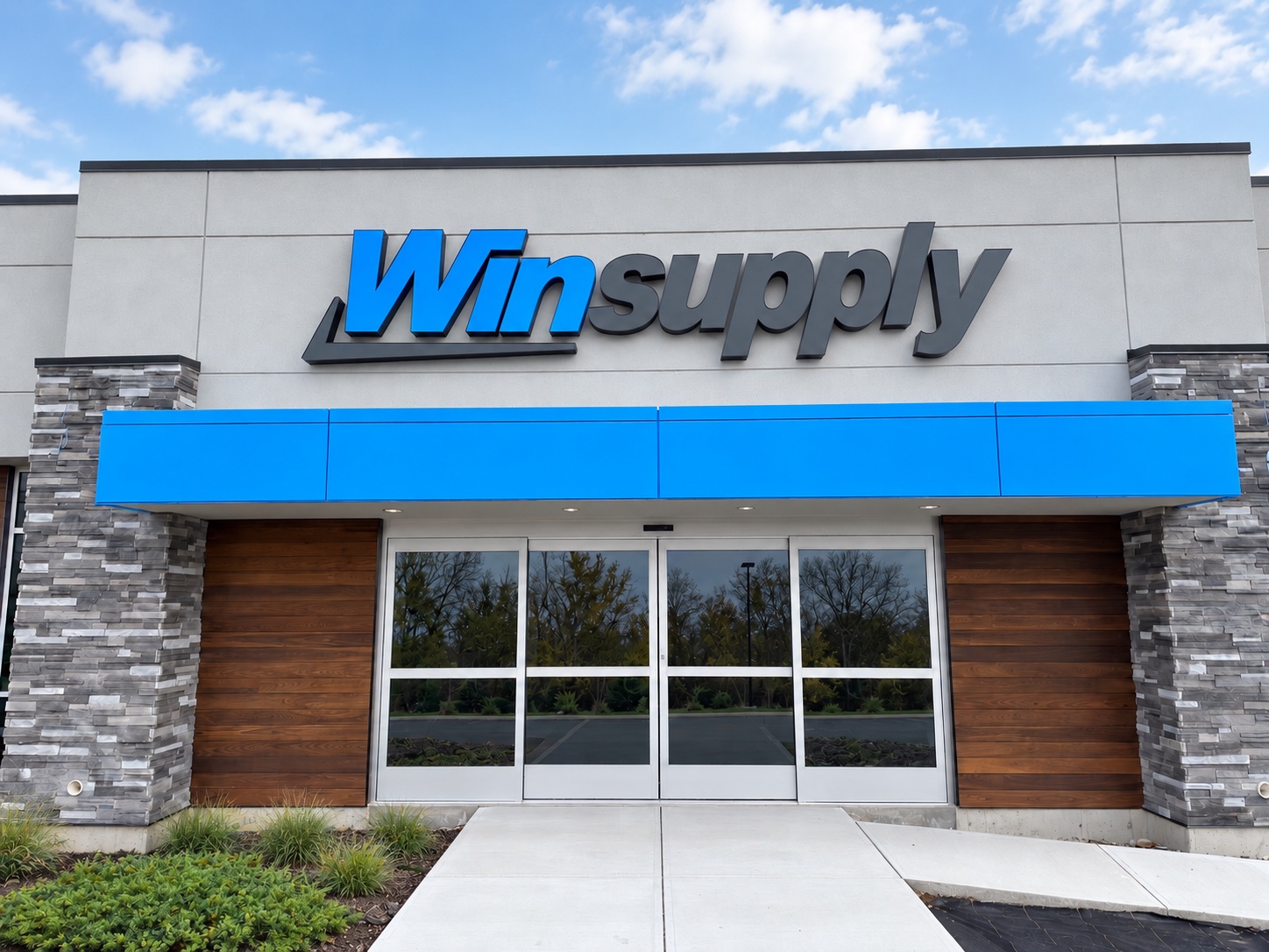 The complete Winsupply storefront with blue and charcoal exterior lettering, stone columns and landscaped entrance